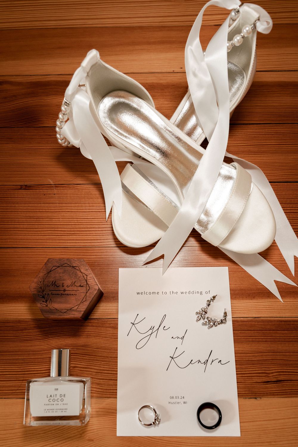 Wedding details flatlay with white shoes, invitation cards and perfume bottle on wooden background.