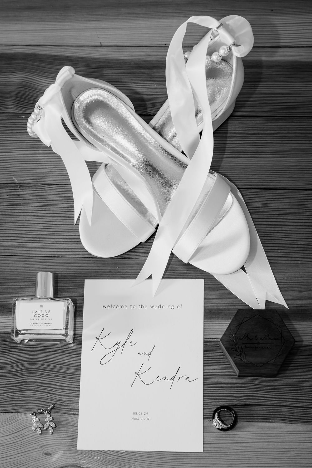 Black and white wedding detail shot of bridal shoes and invitation suite on wooden surface.