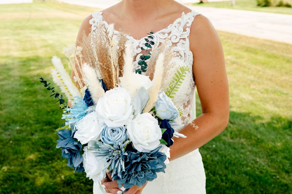Wedding bouquet featuring white roses and dusty blue accents against a lace wedding dress.