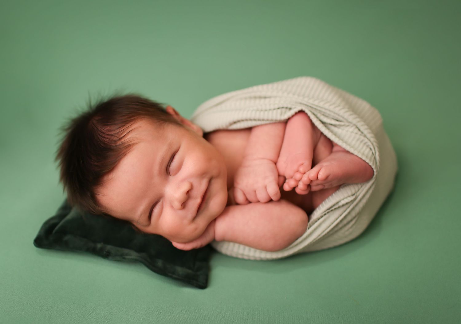 Baby boy snuggled and wrapped in green and smiling in Alvin, Tx photography studio