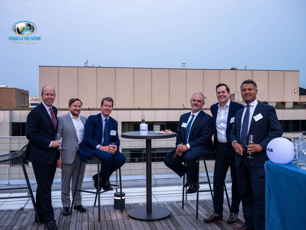 Corporate event attendees gathered on a rooftop patio with tables and chairs during a daytime function.