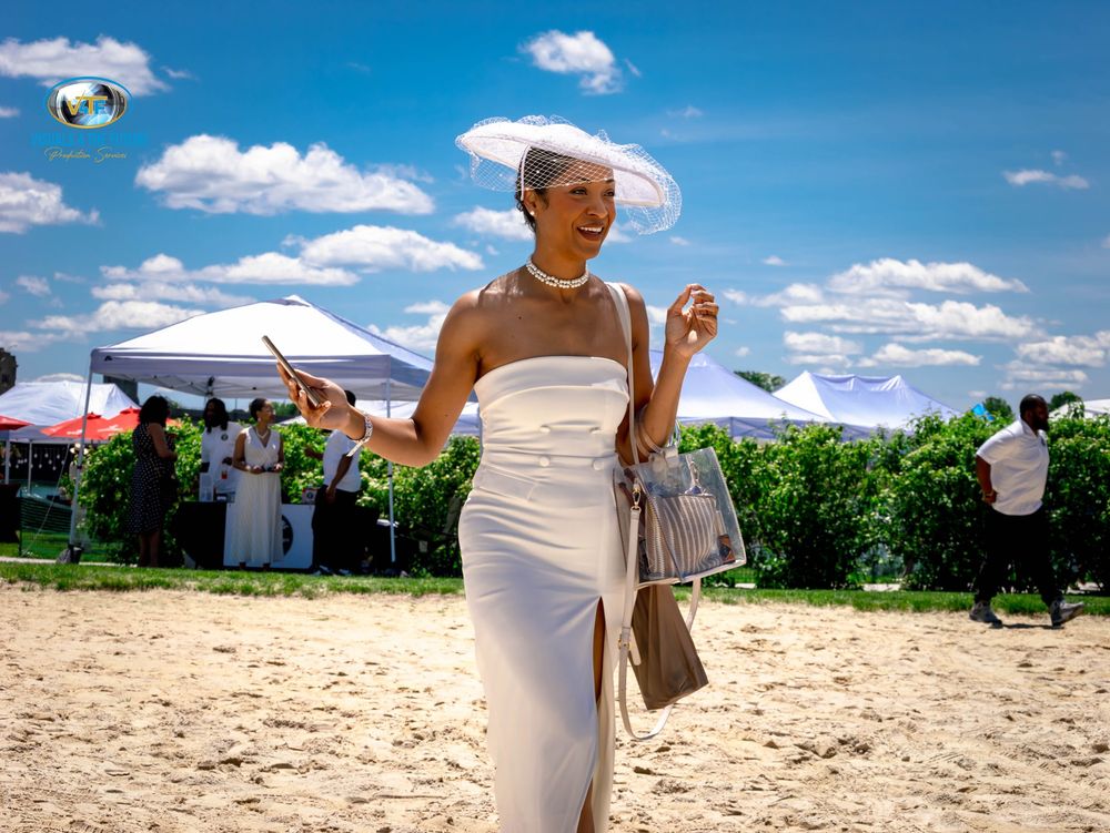 A panoramic view of a beach wedding ceremony setup with white chairs and decor against a bright blue summer sky.