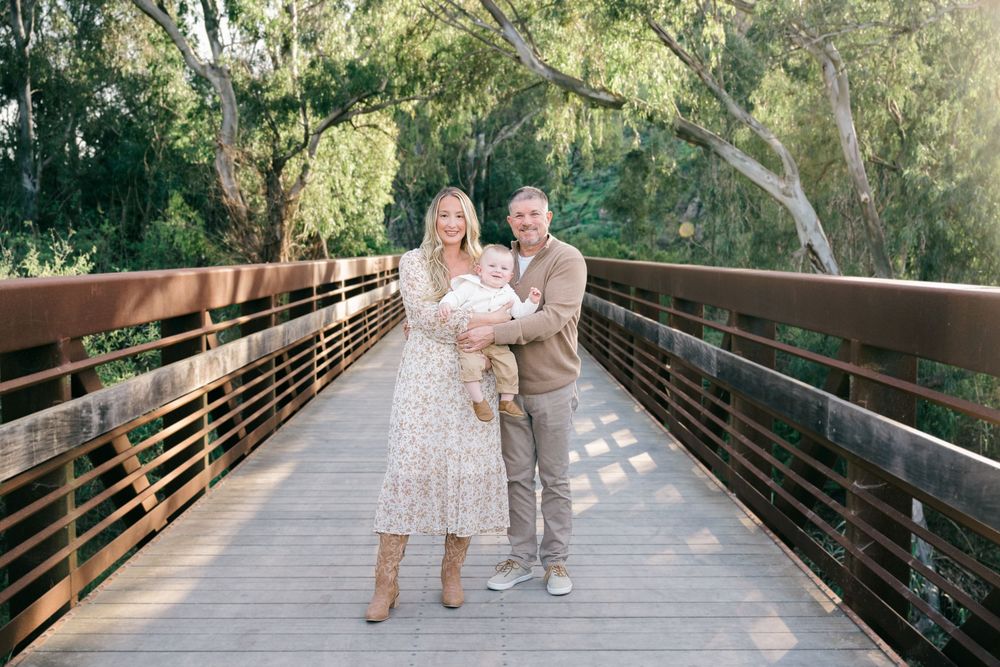 A couple walks together on a wooden bridge pathway surrounded by lush green trees and natural scenery.