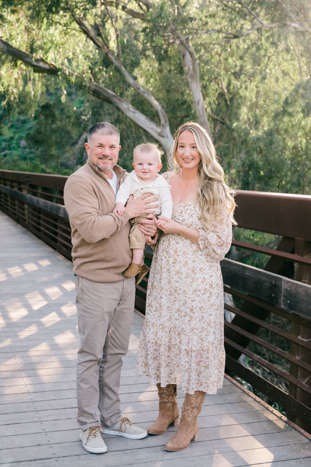 Family portrait session on wooden bridge with brown and floral outfits in natural outdoor setting.