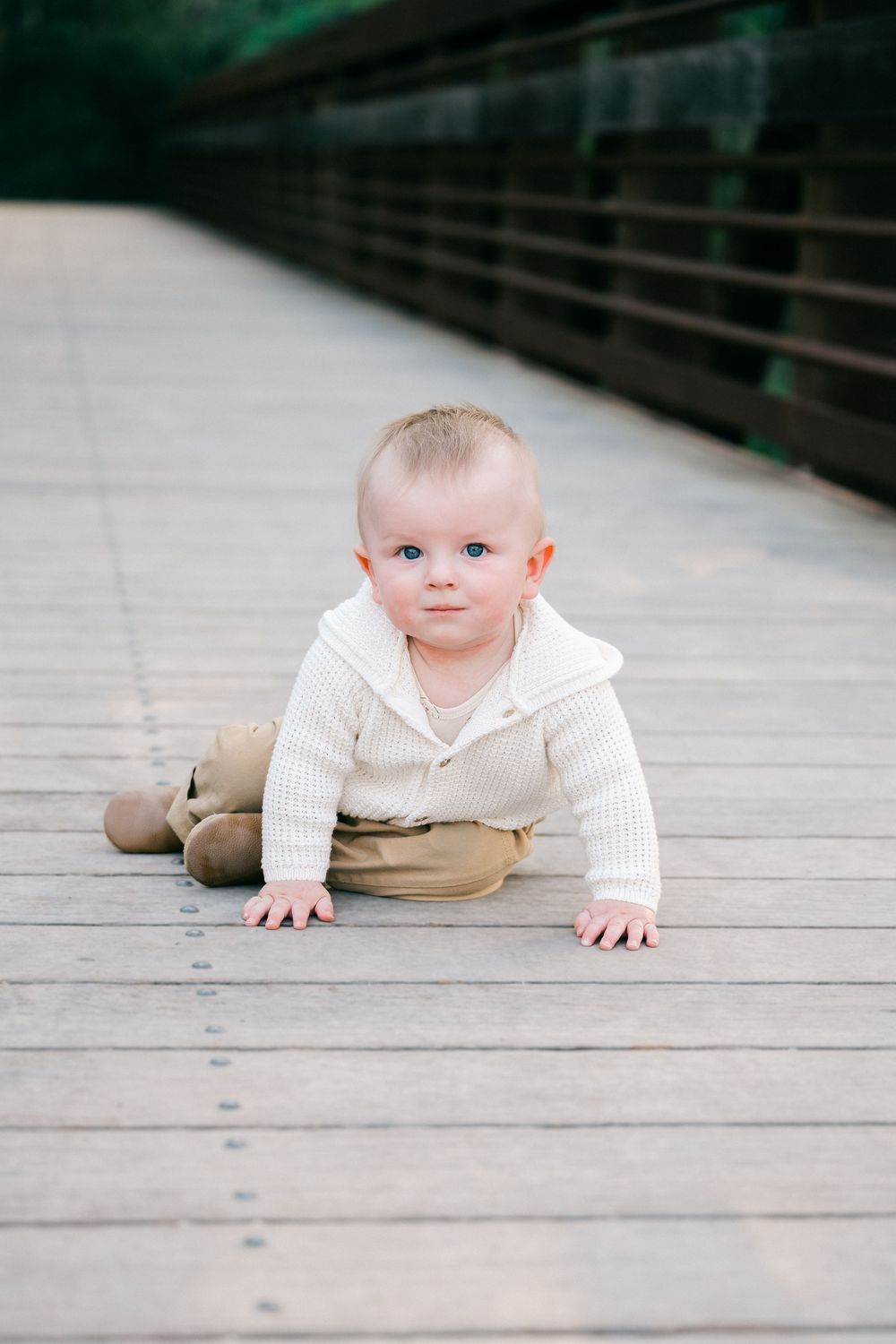 A baby in a cream-colored outfit crawls on a wooden deck in a sequence of progressive movement photos.