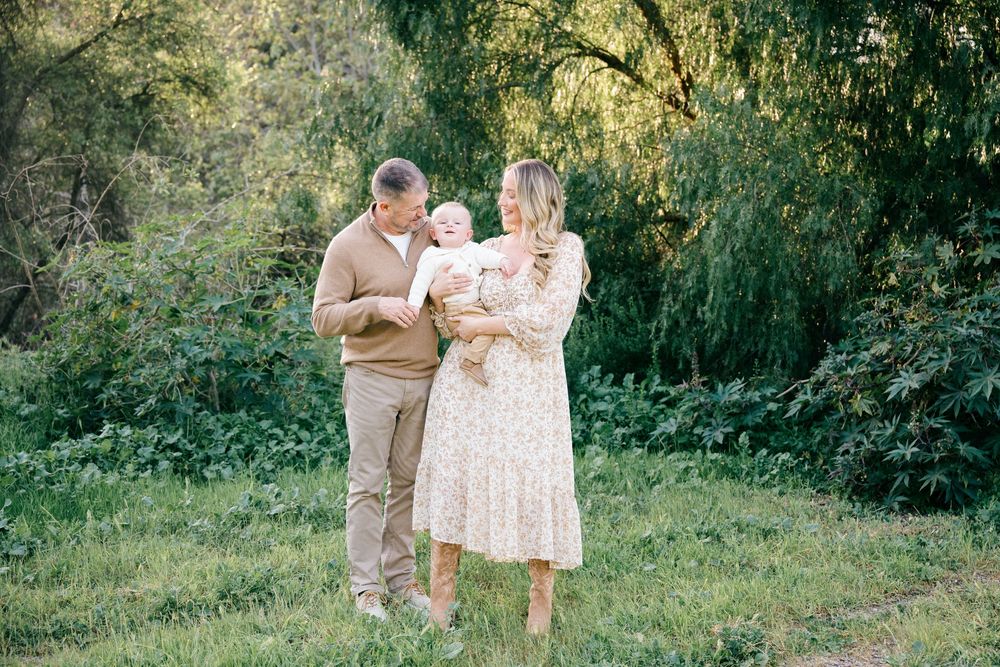 A couple embraces in a sunlit garden setting wearing coordinated beige and white outfits during a romantic photoshoot.