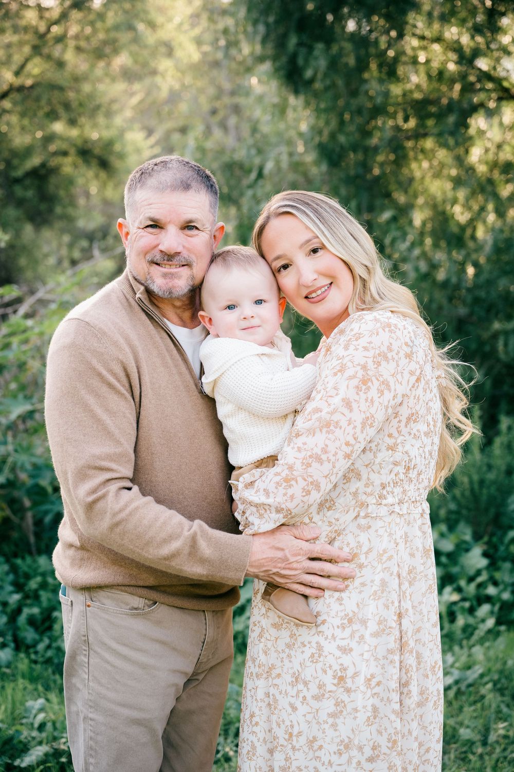 A heartwarming family portrait taken outdoors with natural greenery in the background.