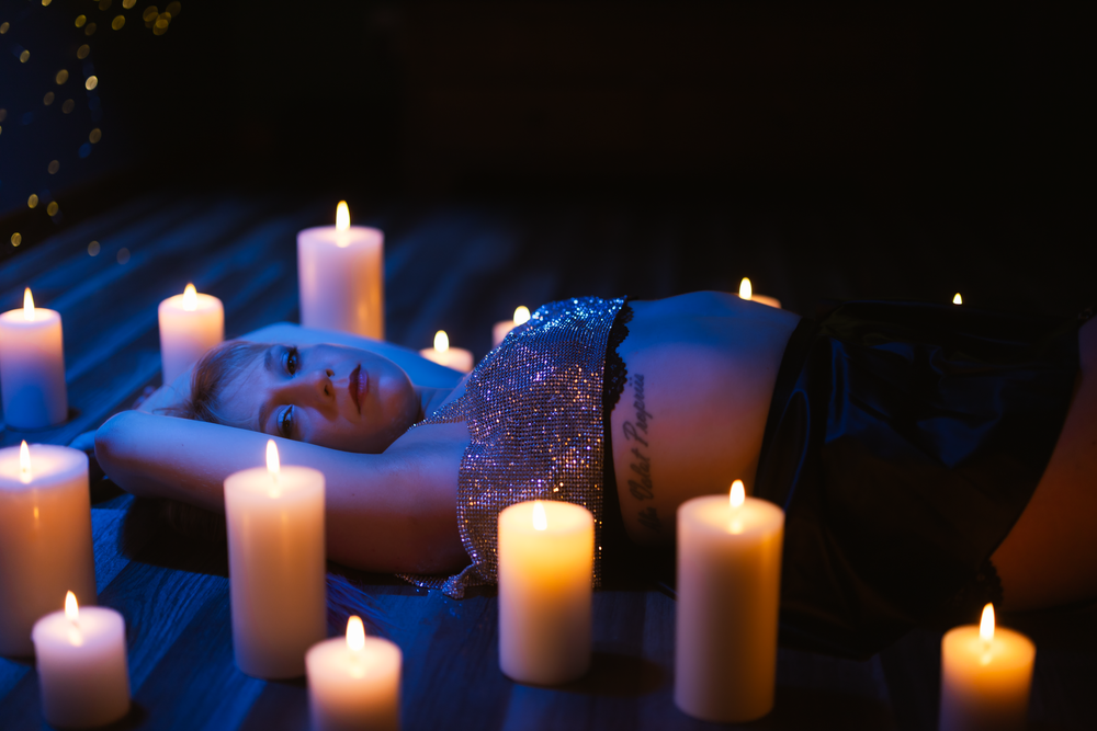 As she lays there surrounded by candles with a blue hue she waits patiently