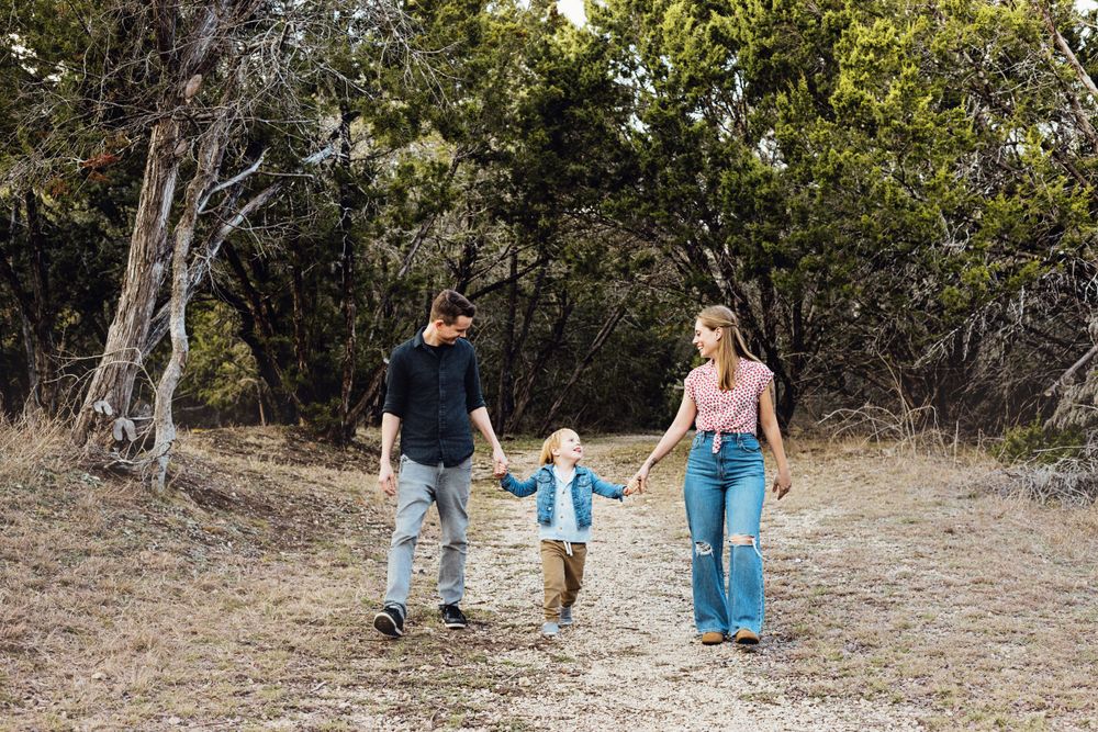 Family walks together holding hands on a forest trail on a sunny afternoon.