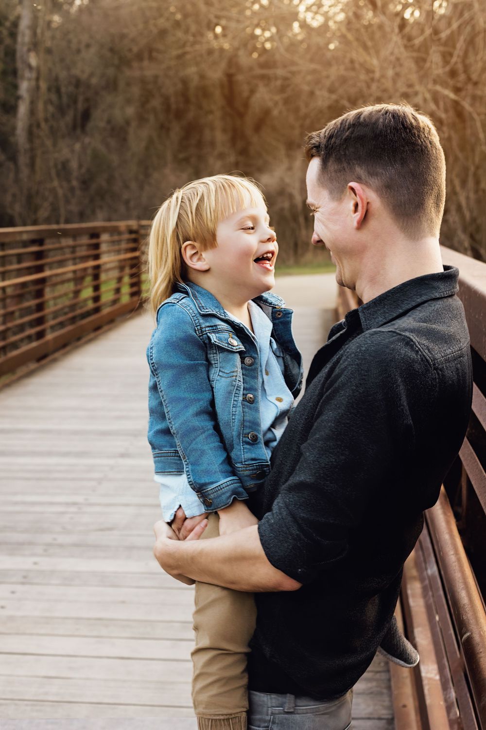 A tender moment shared between parent and child laughing together on a wooden bridge in autumn.