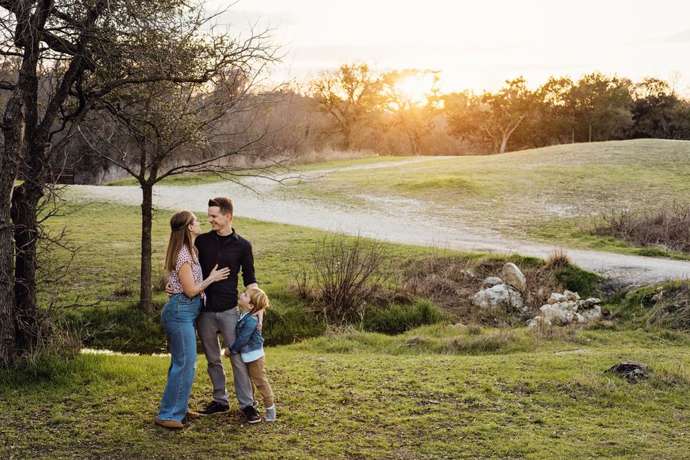 A parent and child walk together on a grassy hillside path at sunset with warm golden light filtering through trees.