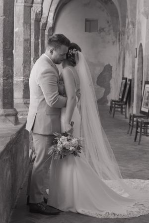A black and white portrait of a bride and groom having a hug. The bride is holding her bouquet down to the side.