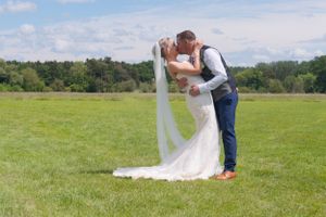 Newlywed bride and groom having a dip kiss in an open field. The brides veil is flying behind her.