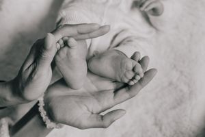 Black and white, mum holding the feet of newborn baby.