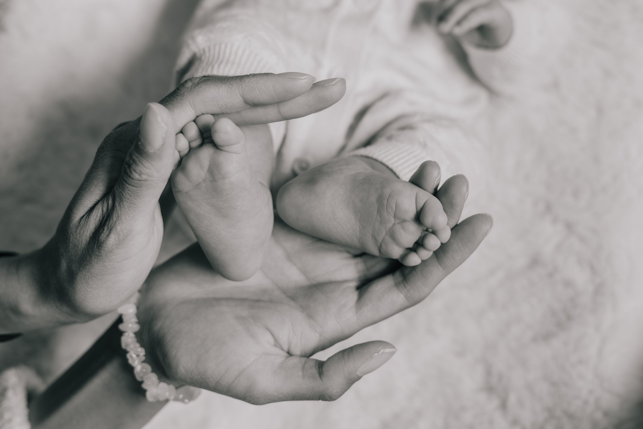 Black and white, mum holding the feet of newborn baby.