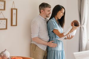 New parents holding their newborn baby in front of them, in the babies nursery.