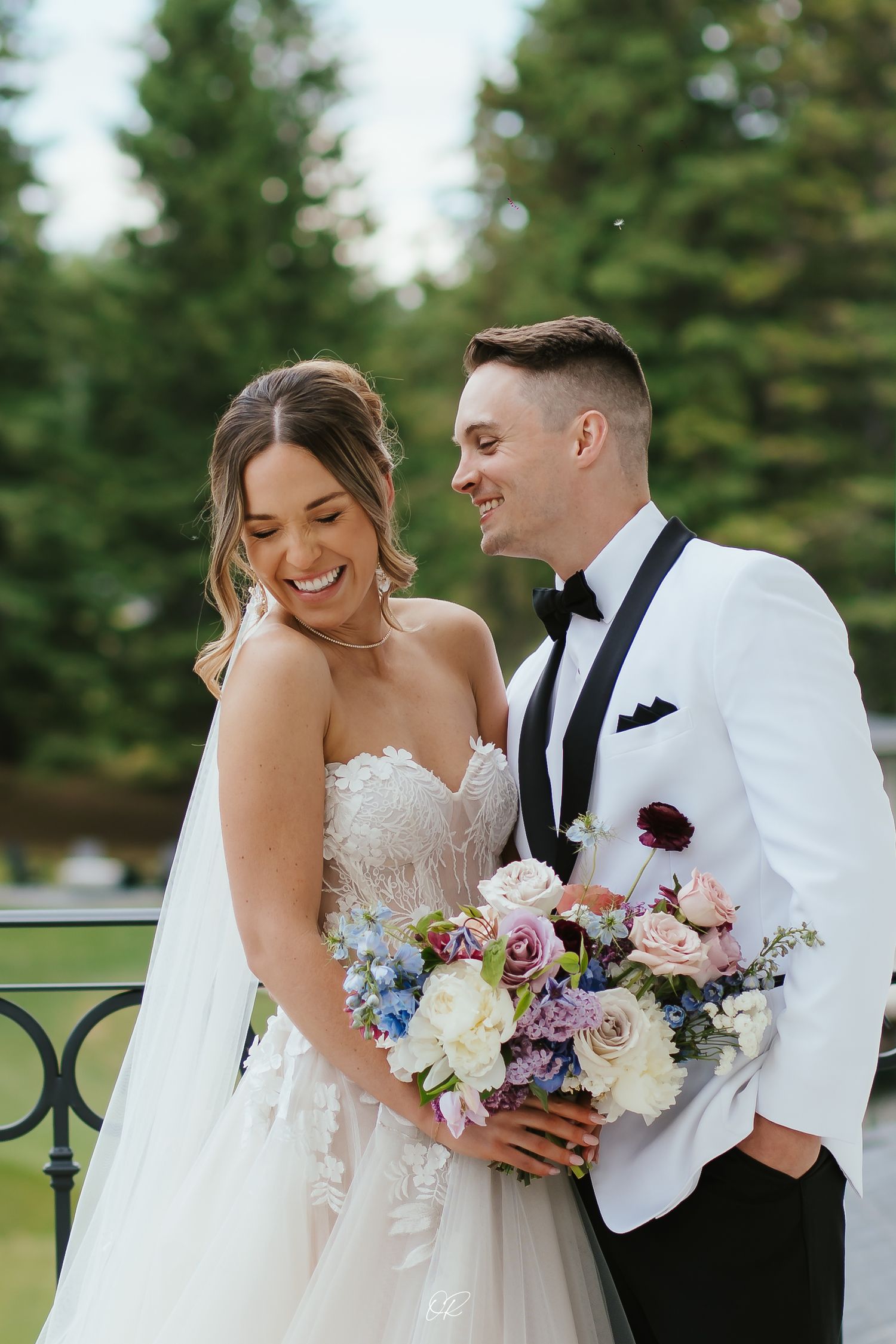 A happy couple shares a joyful moment at their wedding, with the bride holding a beautiful bouquet of mixed pastel flowers.