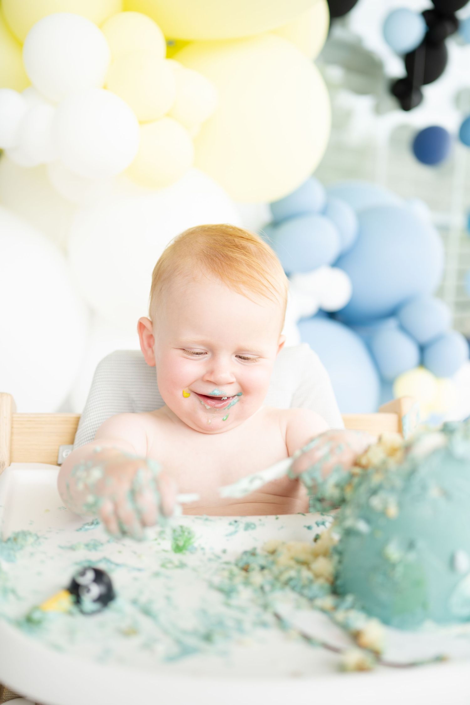 little boy in white knit jumper and bonnet looks up towards the light for his first birthday session