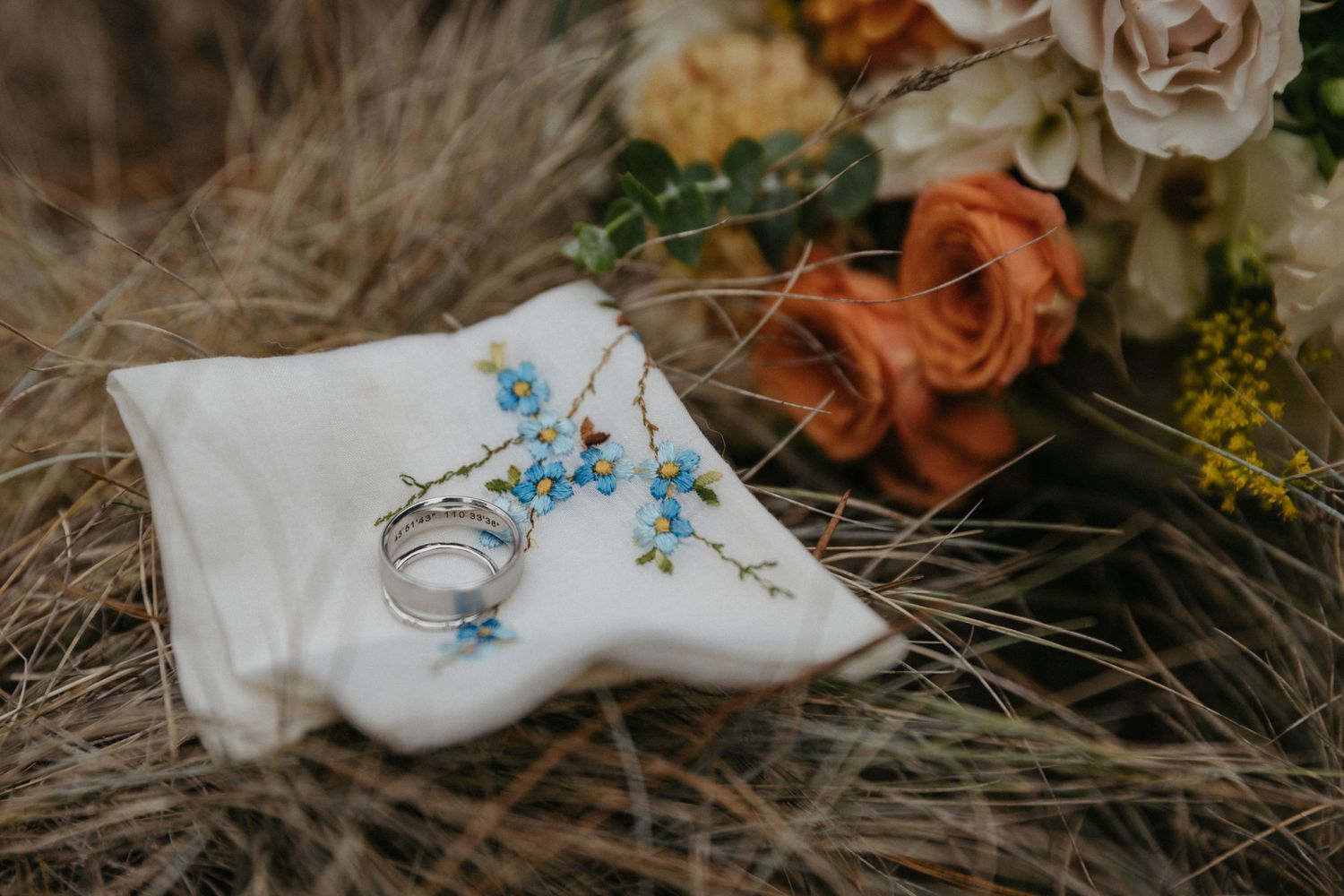 Wedding rings and delicate embroidered details on white fabric with roses.