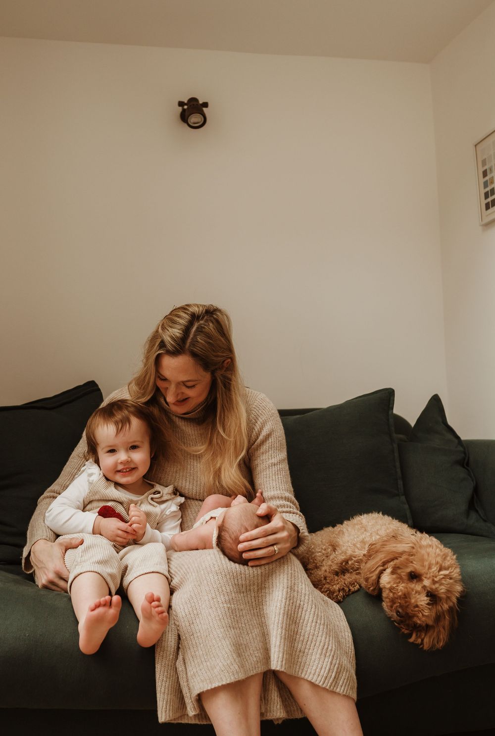 A cozy family moment on a dark green couch with a sleeping goldendoodle dog curled up beside them.