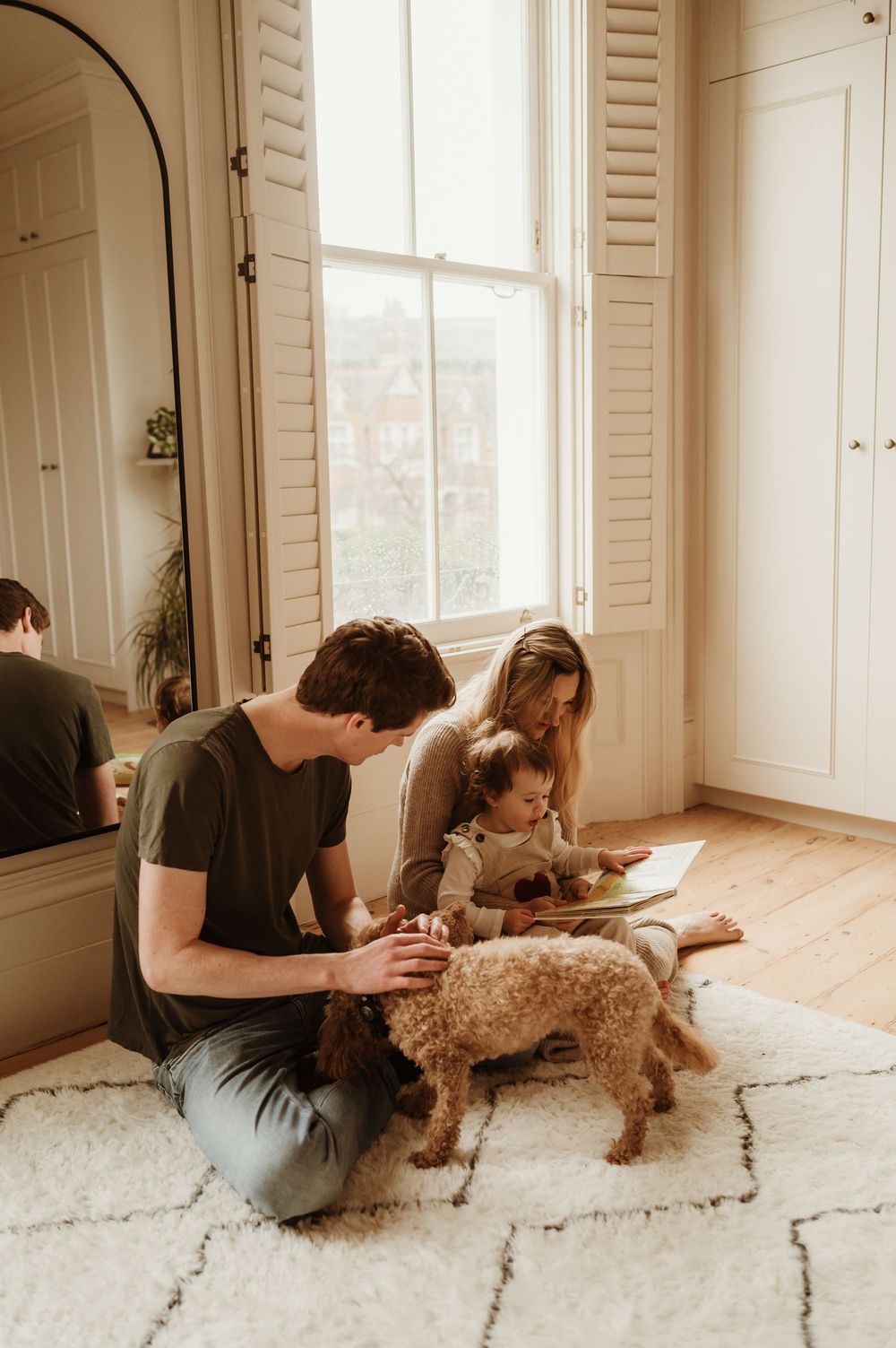Family spending quality time together reading on a cozy white rug with their fluffy brown dog near a bright window.