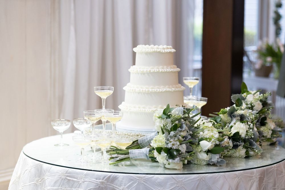Elegant white wedding cakes and floral arrangements displayed on glass tables at a luxurious reception venue.