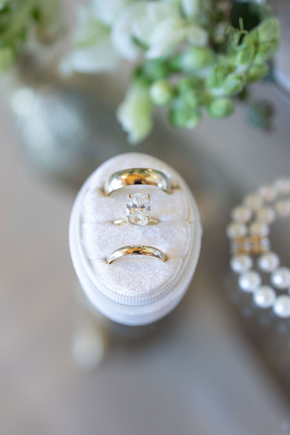 Wedding rings displayed on white textured ring holders in a soft, elegant setting with delicate floral accents.