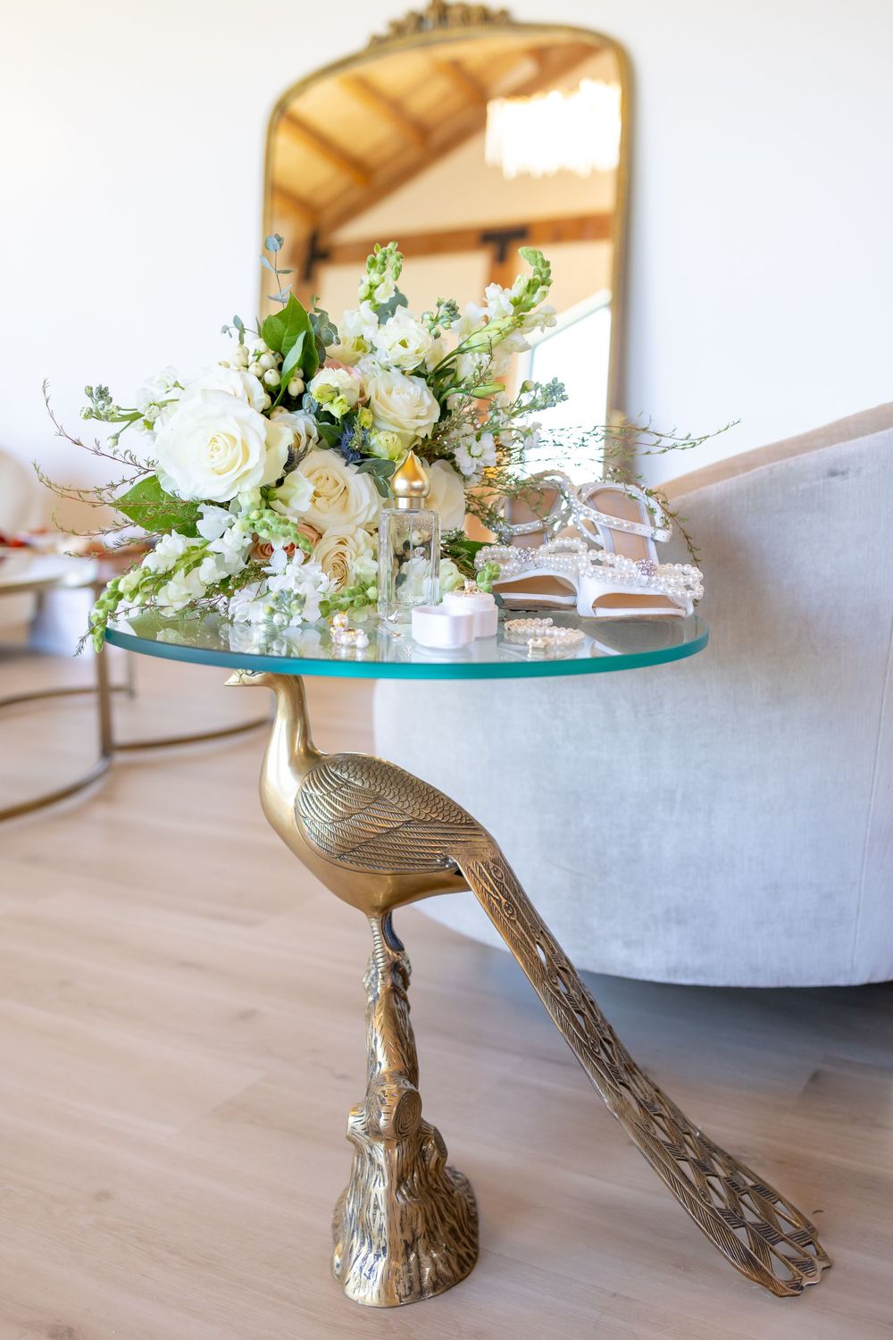 Glass cake stand with ornate gold branch-like pedestal displays white floral arrangement on wooden table.