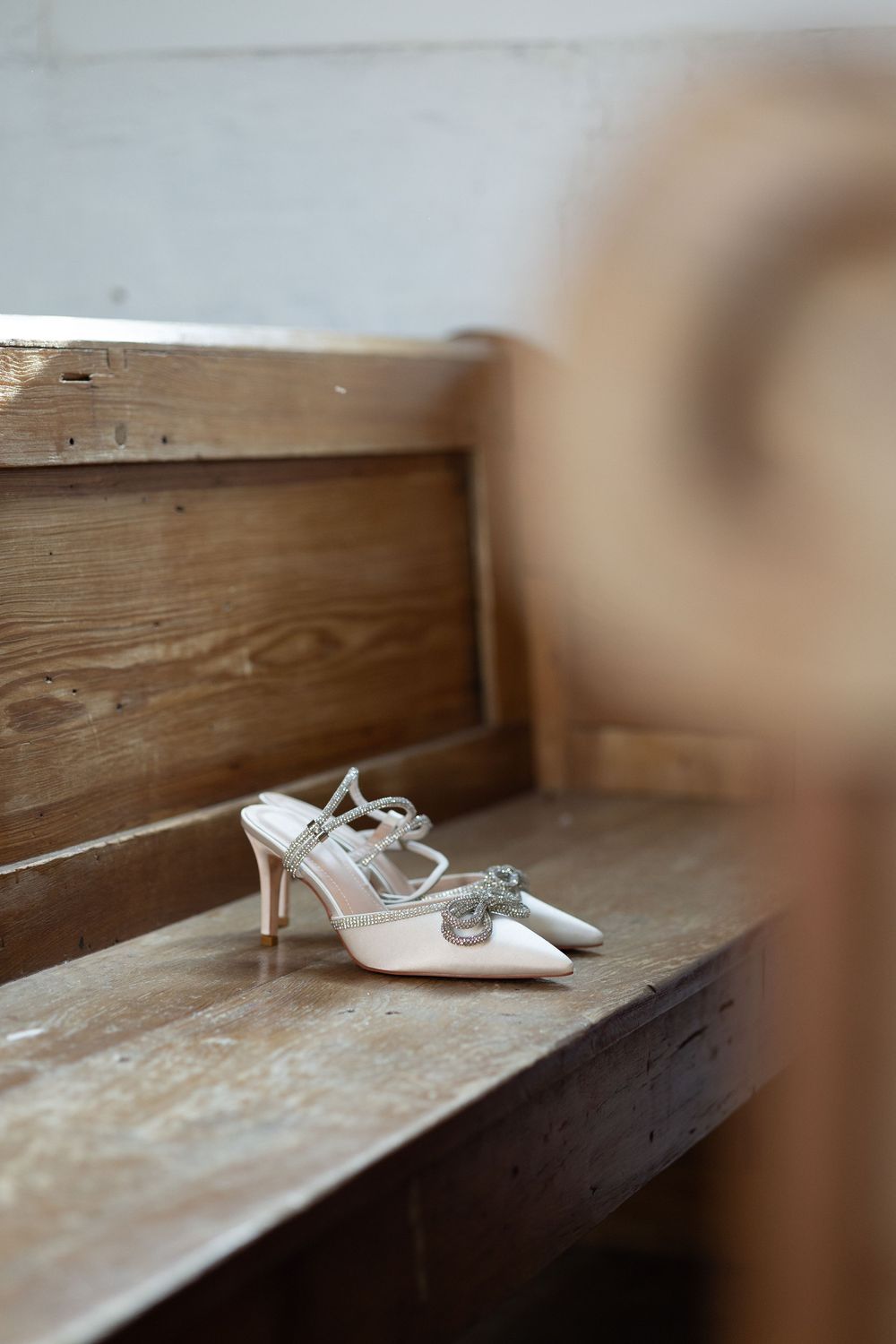 A pair of elegant white bridal or wedding shoes sitting on a rustic wooden bench or shelf.