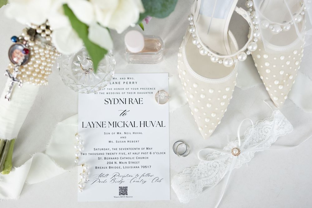 Soft white and cream colored decorative items including lace, pearls, ribbons and vintage paper arranged in an elegant flat lay.