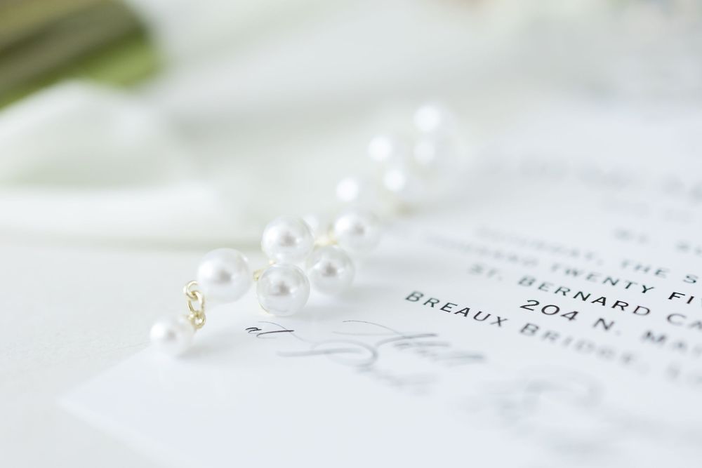 Delicate seashells and pearls arranged with wedding rings and decorative elements on white textured surface.
