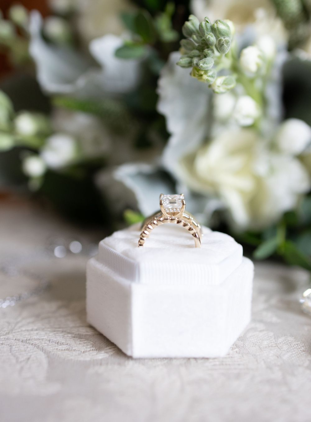 A geometric white wedding ring box shown in a series of angles with soft floral elements in the background.