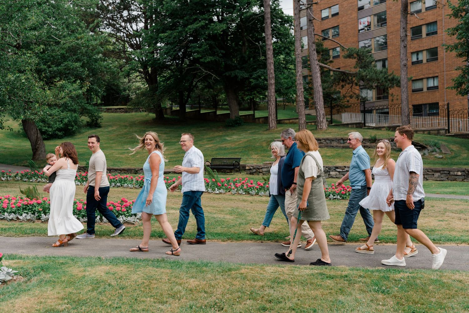 Extended family group walks together along a garden path surrounded by trees and colorful flowers at Dartmouth Commons.