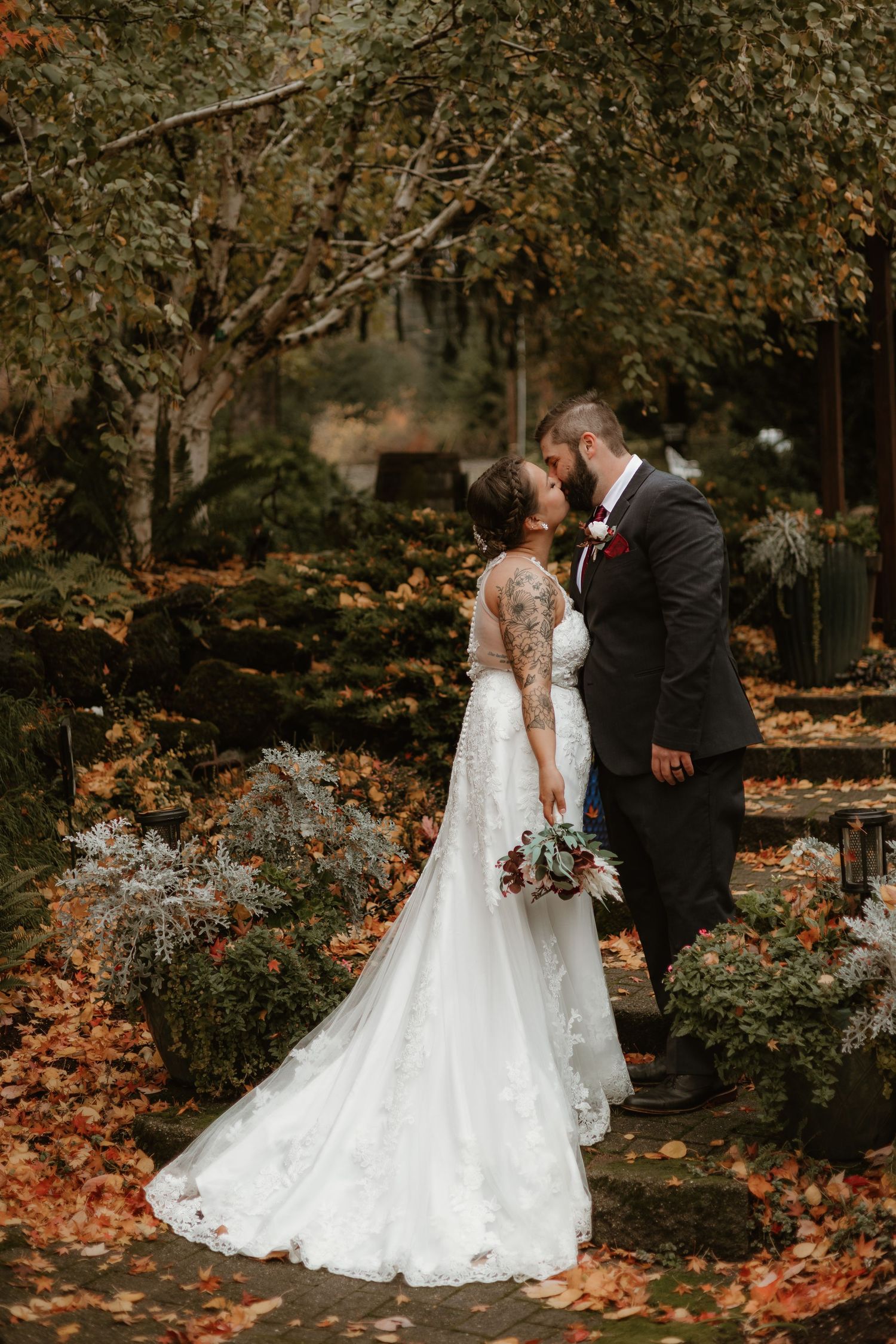 A romantic autumn wedding scene with a couple kissing among fallen leaves and foliage.