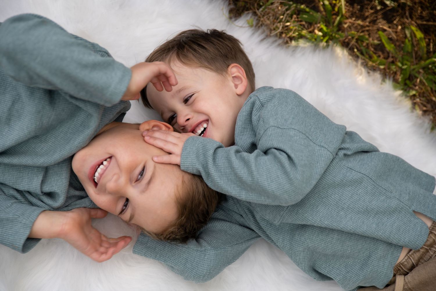 Sweet candid moment between two in matching grey outfits lying on white background.