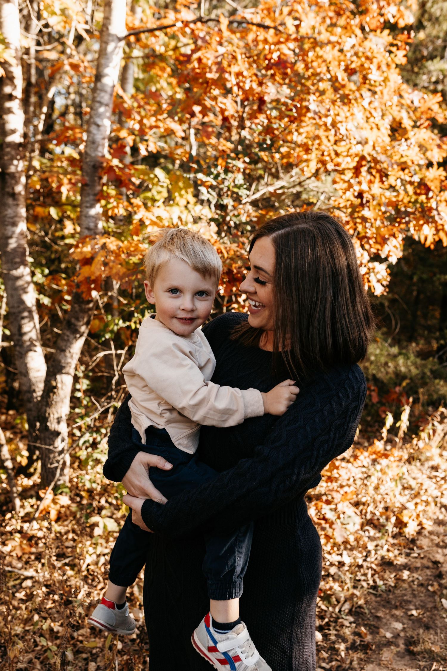 A parent and child share a joyful moment together against a backdrop of golden autumn foliage.