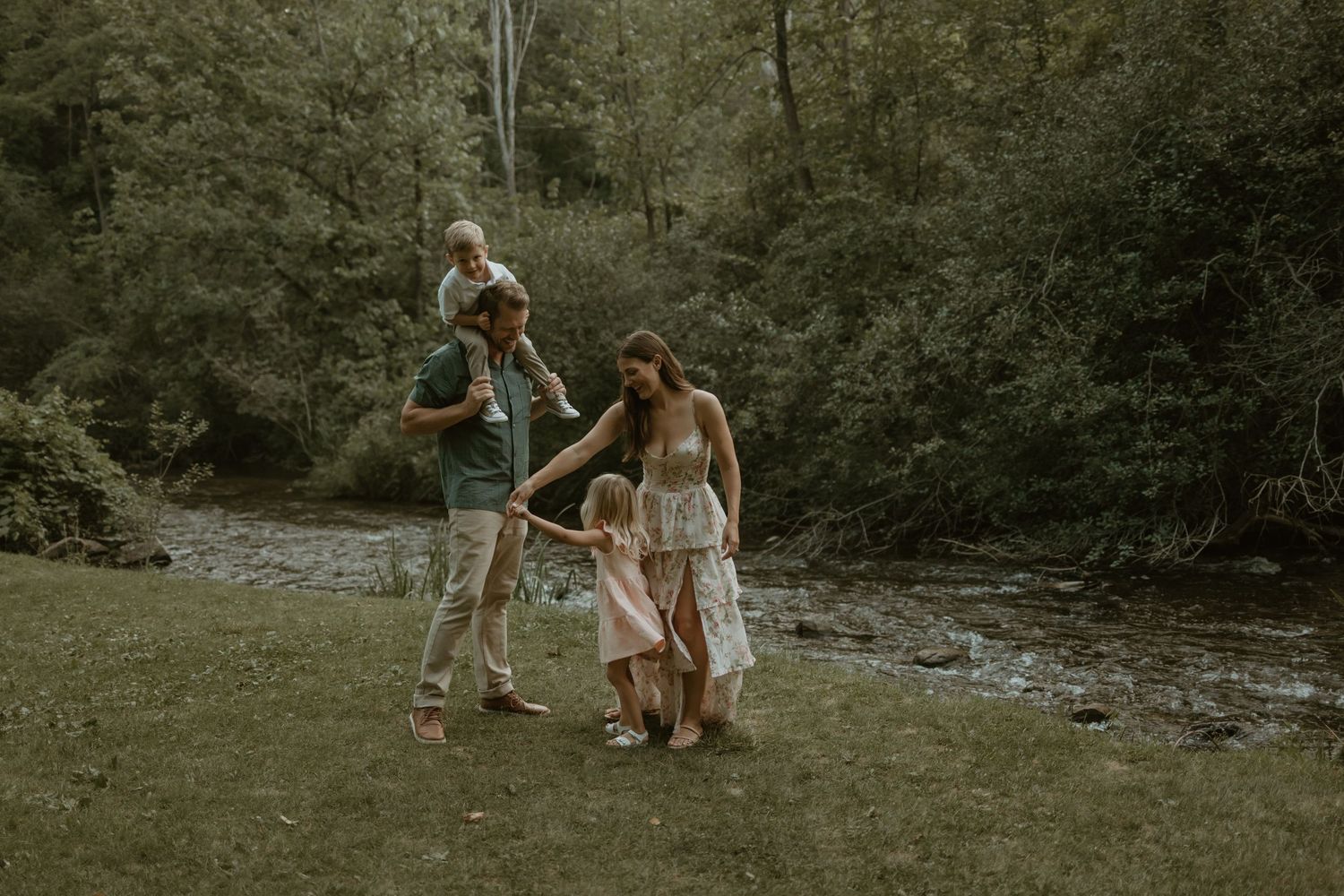 Happy family shares laughter and cuddles while sitting together outdoors among green foliage.