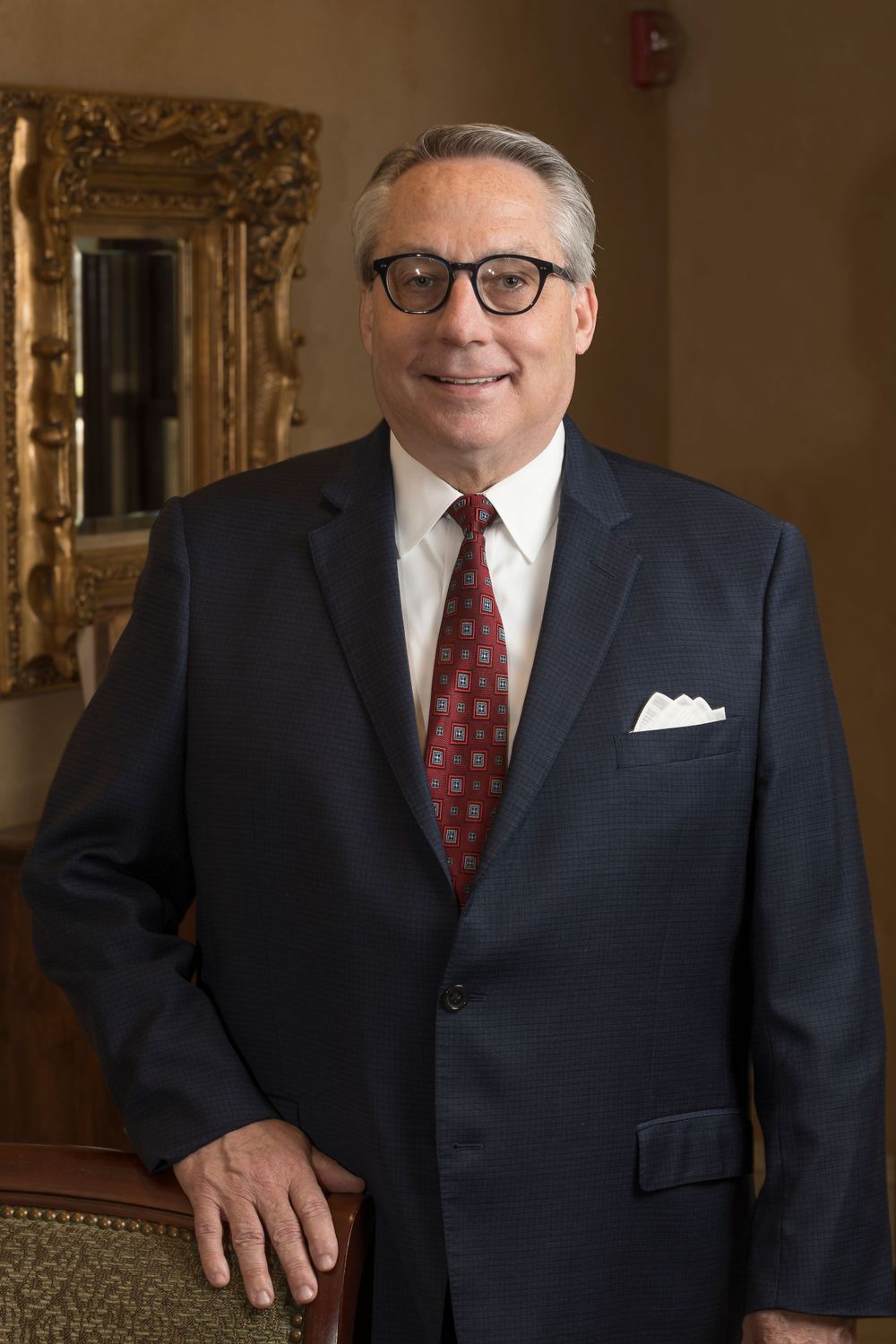 Professional headshot of a person in dark suit with glasses and red tie.