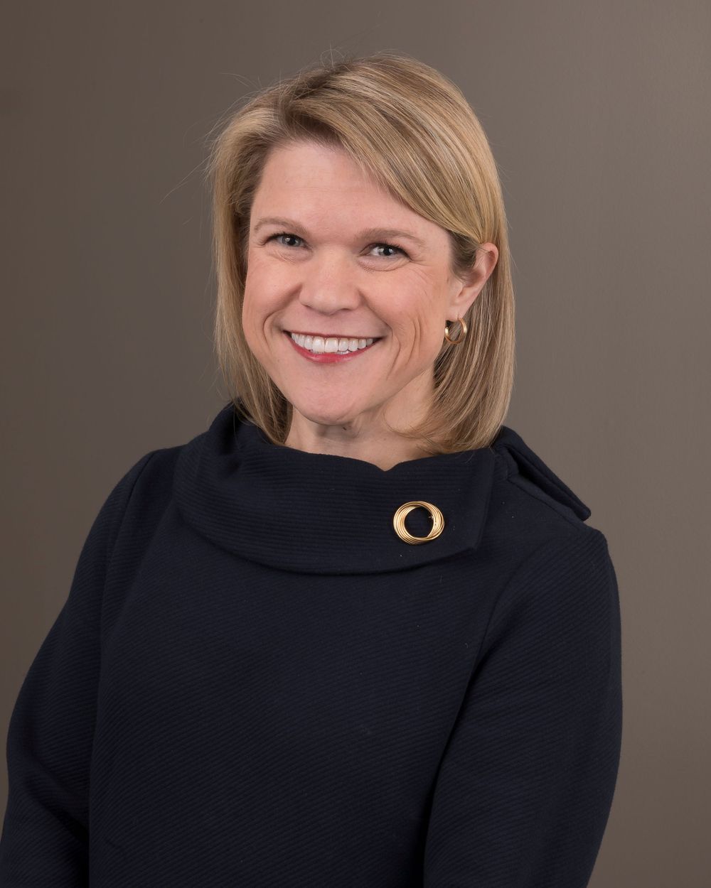 Professional headshot of a person in black attire with a decorative pin.