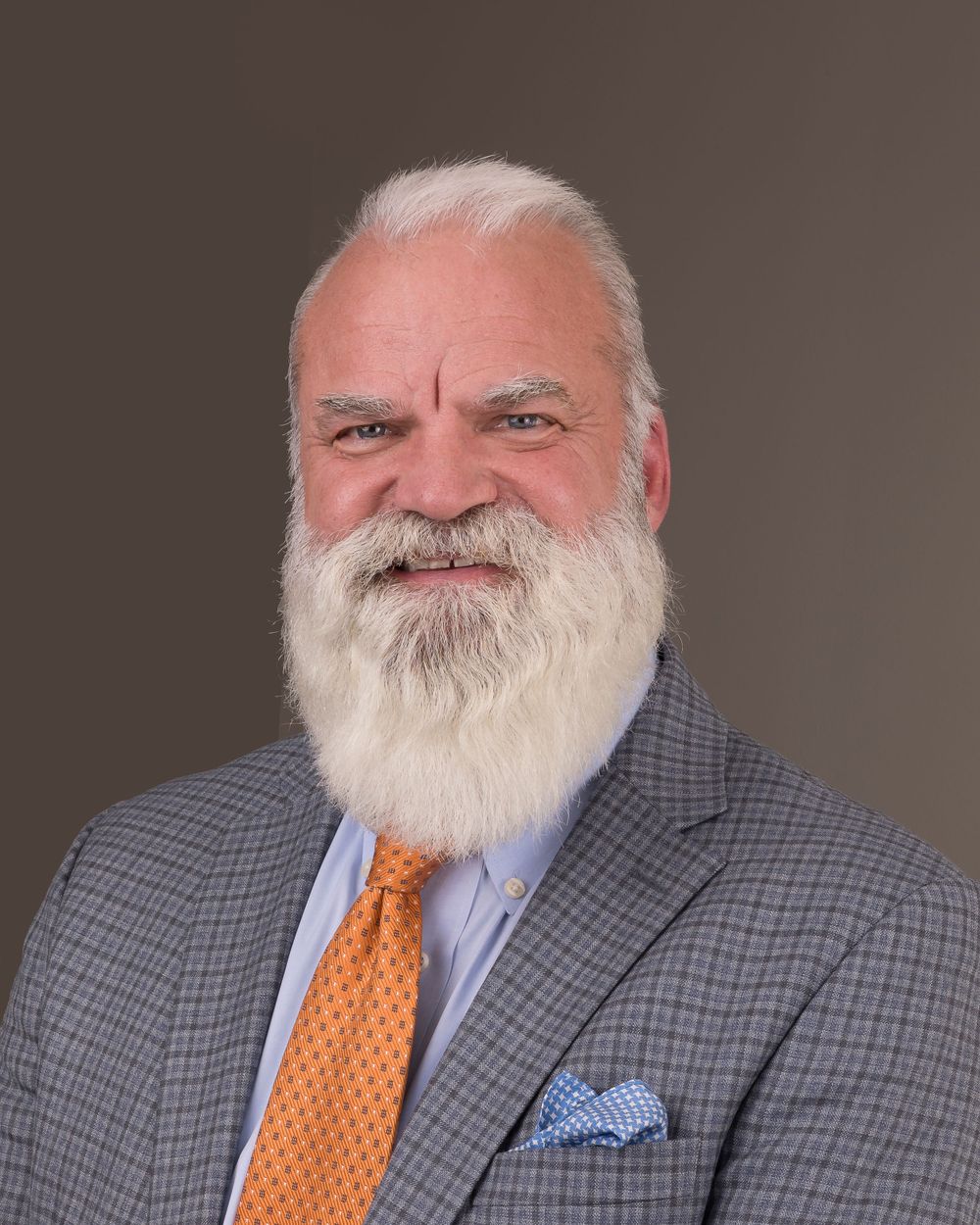 Professional portrait of a person in a checkered suit with white beard and orange tie.