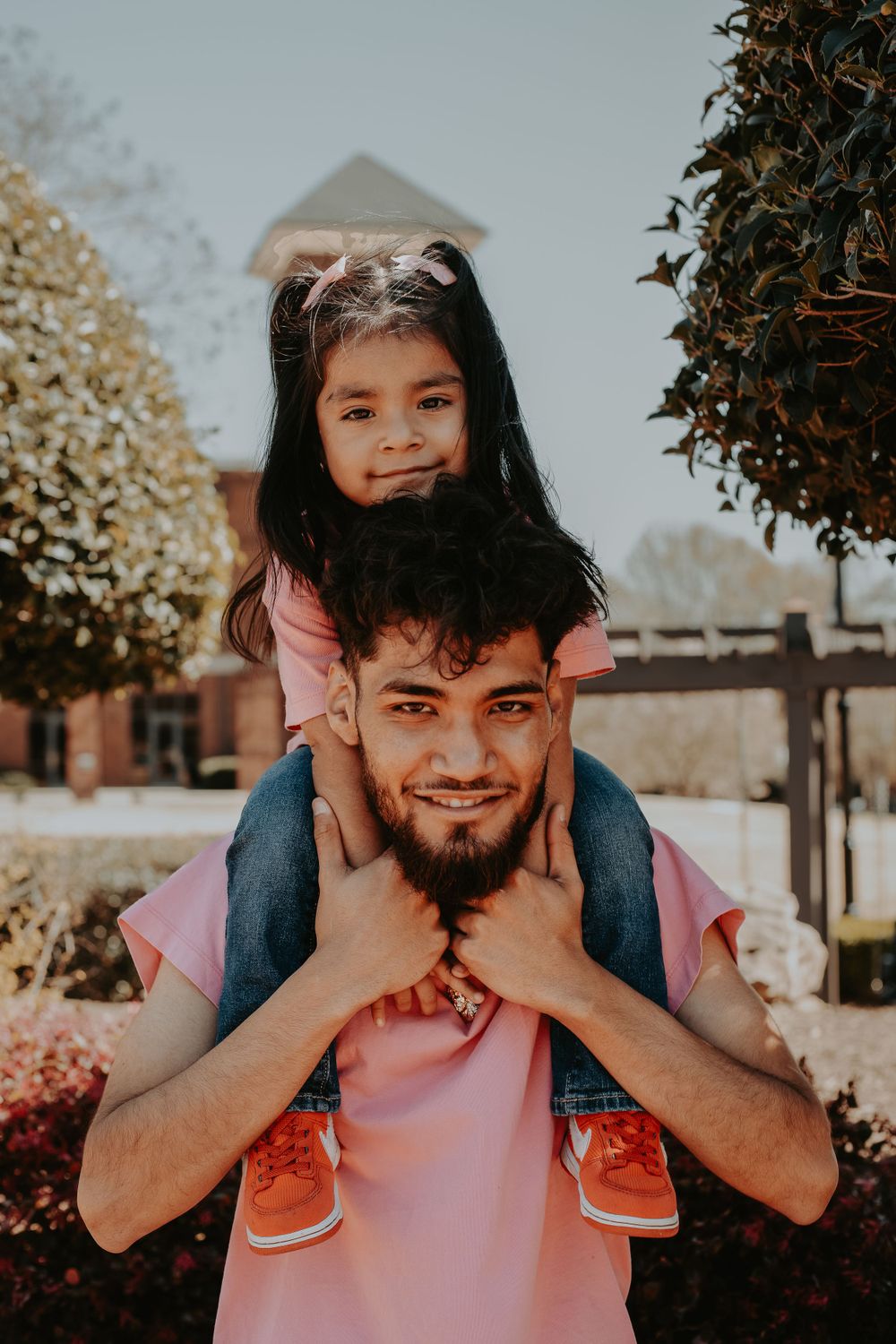 A joyful piggyback ride moment captured outdoors with flowering bushes in background.