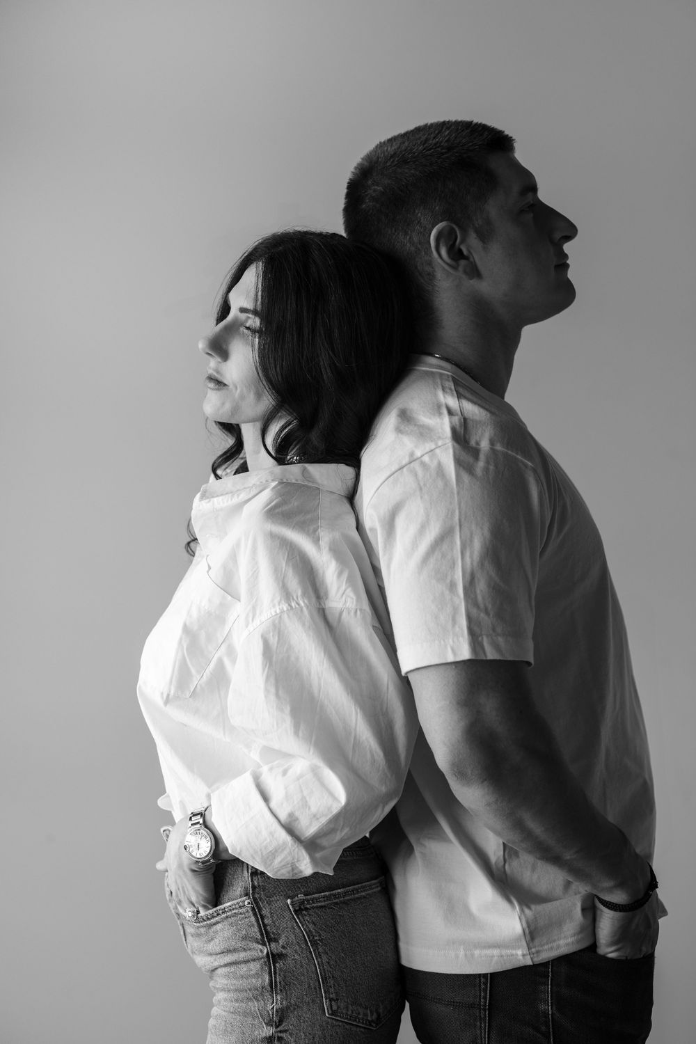 Black and white image series showing two people standing back to back in white shirts and jeans against a plain background.