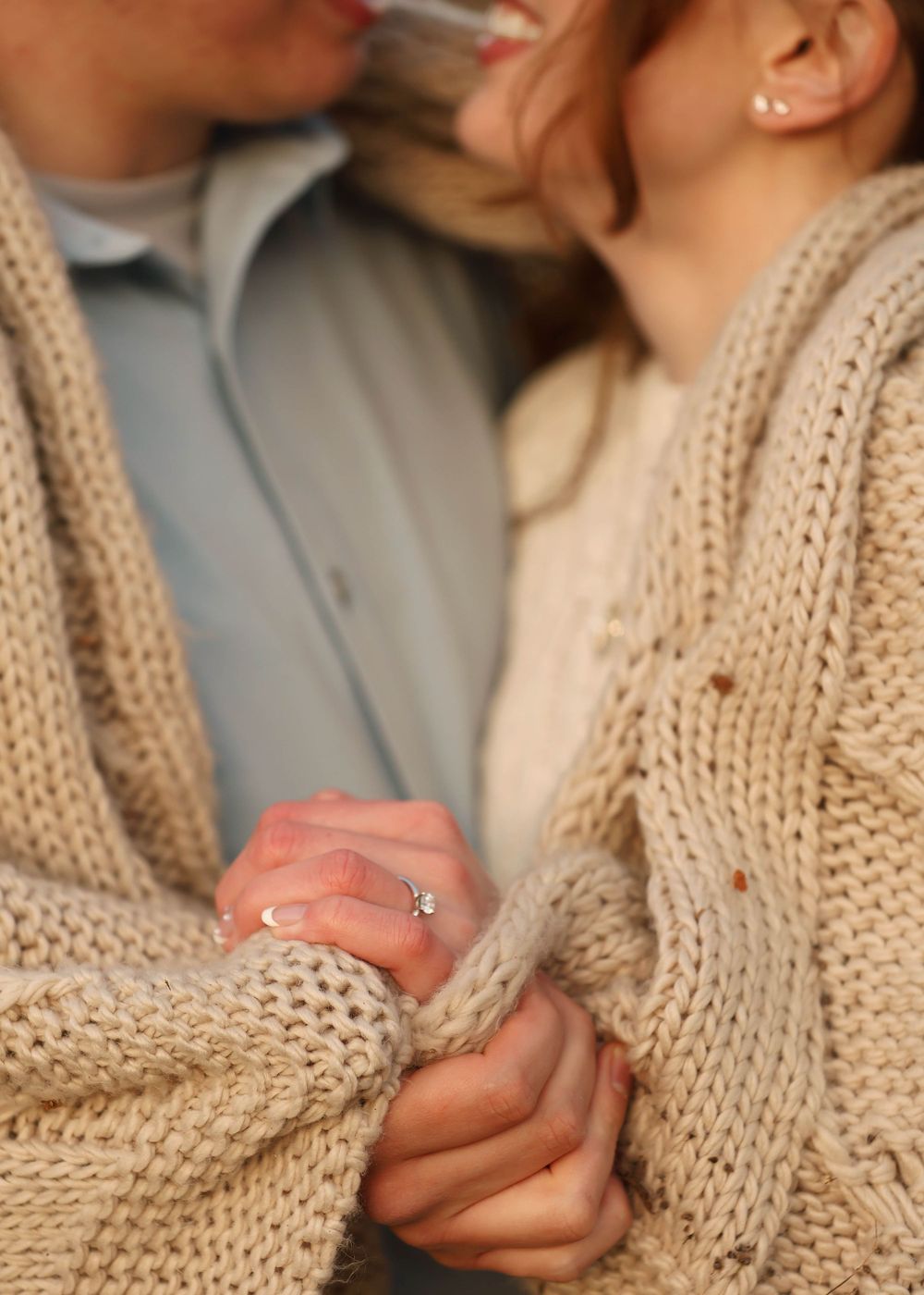 Close-up shot showing hands with engagement ring and cream knit sweater details.
