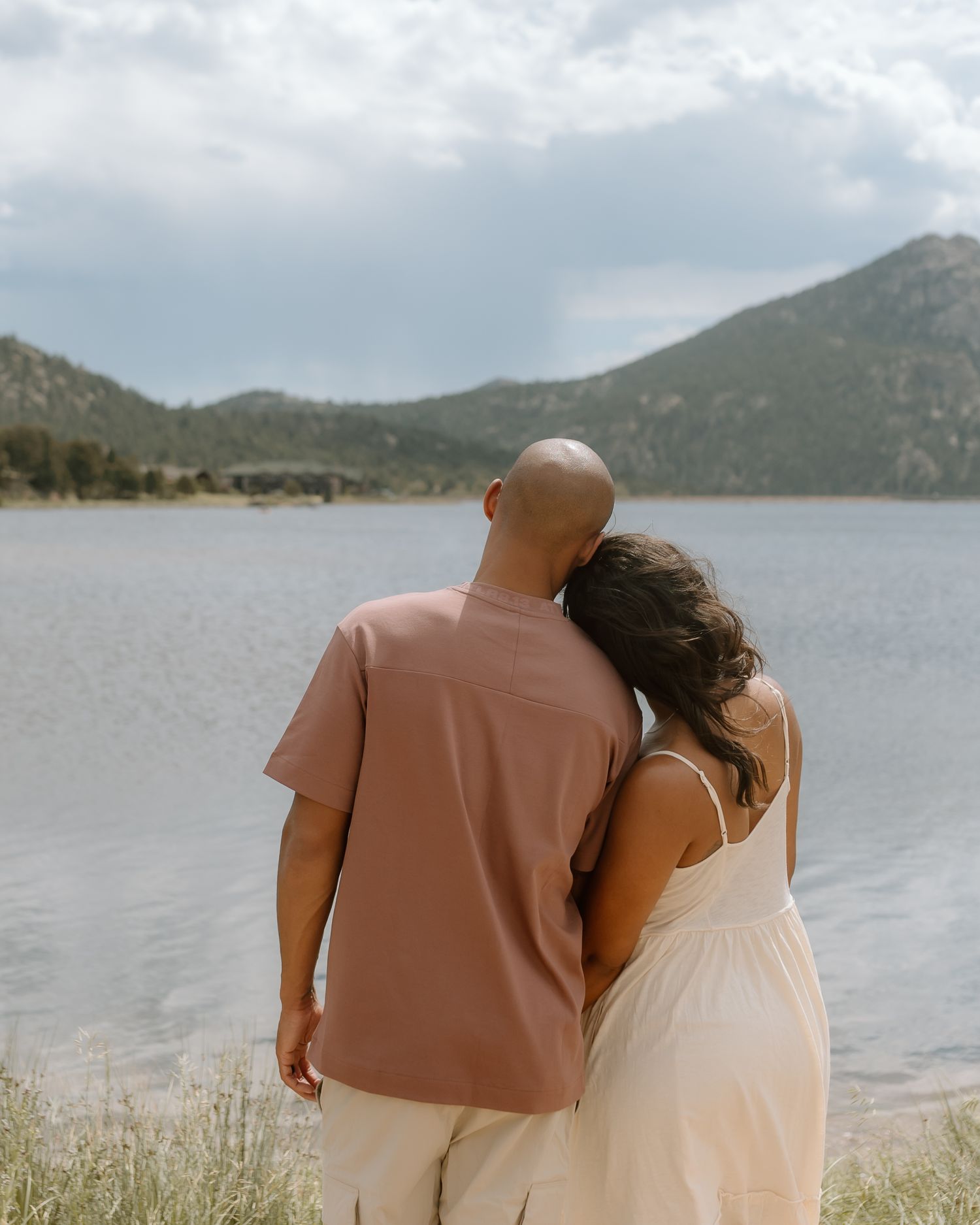 A couple stands together looking out over a scenic mountain lake view in Estes Park Colorado on a cloudy day.