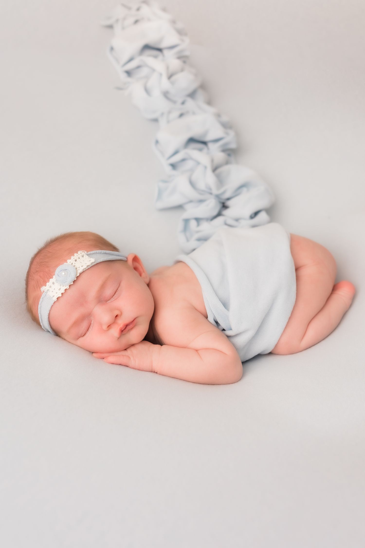 Sleeping newborn baby wrapped in light blue swaddle lying on soft gray blanket.