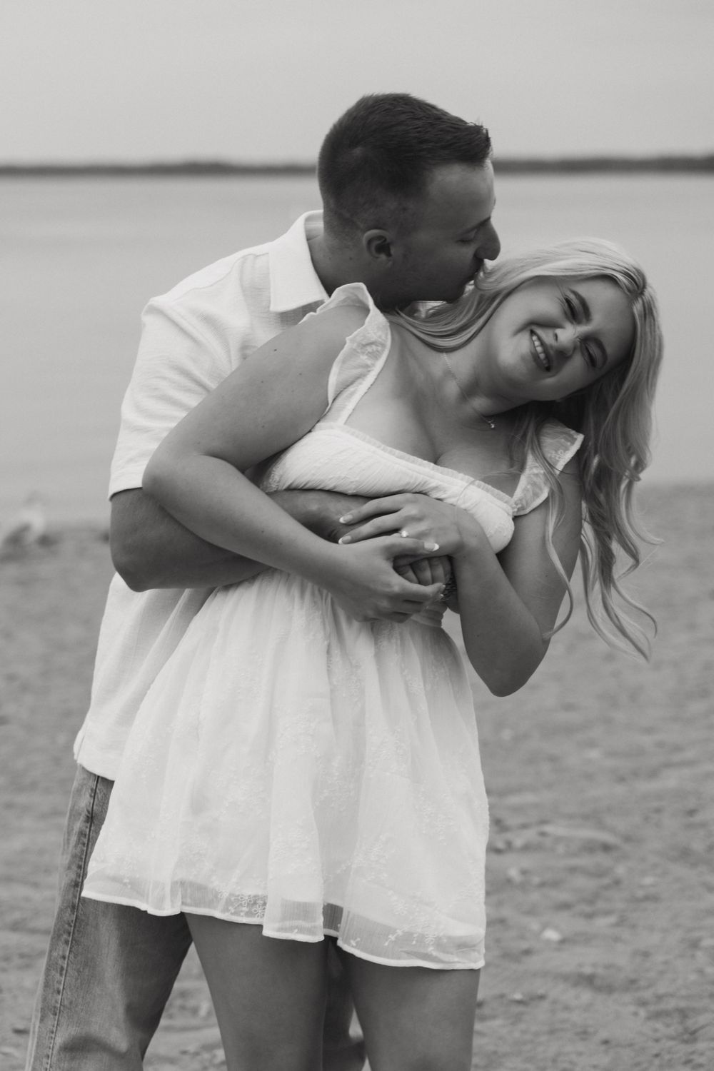 black and white image of couple playing on beach during engagement session
