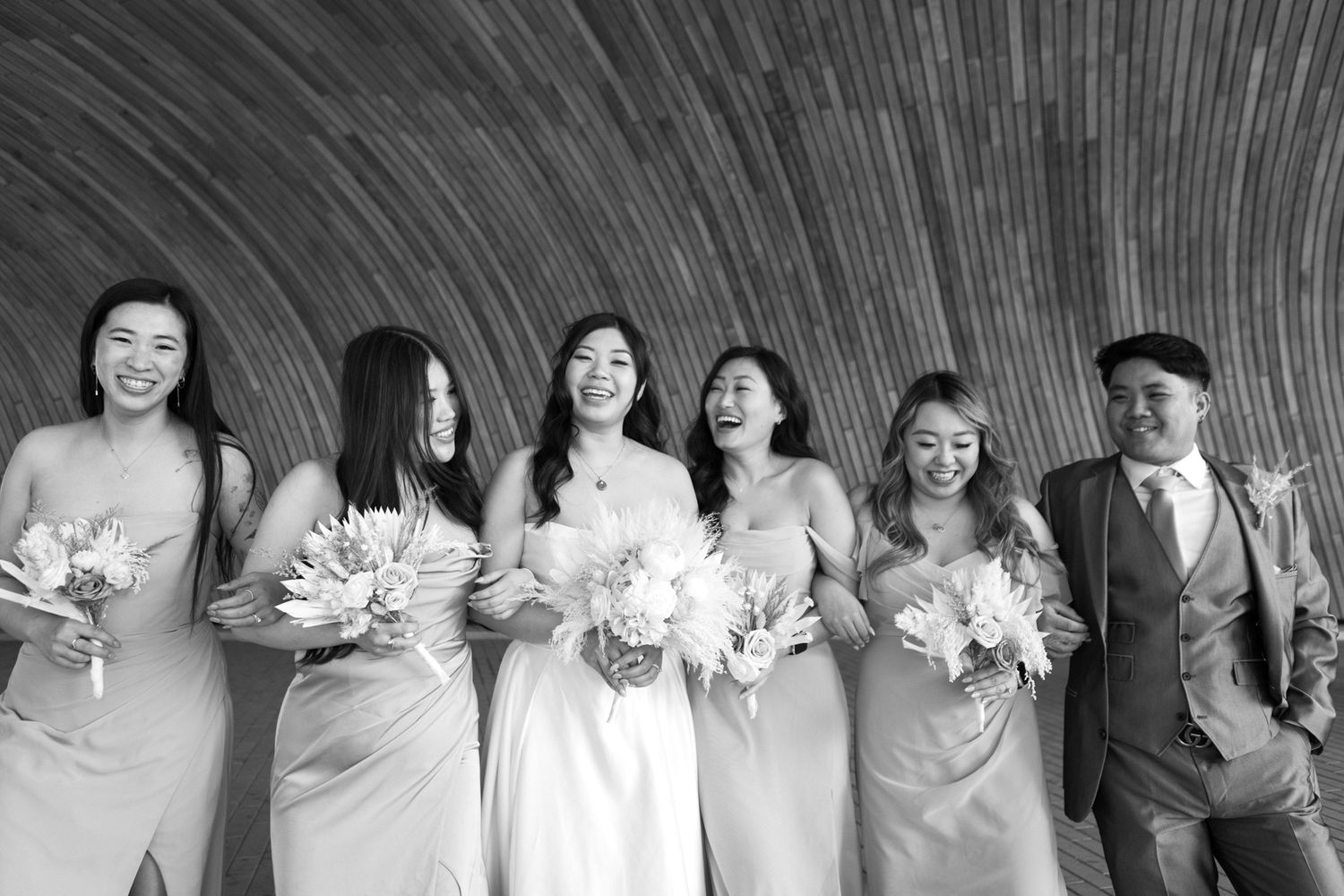 Black and white photo of bridal party lined up against textured wall.
