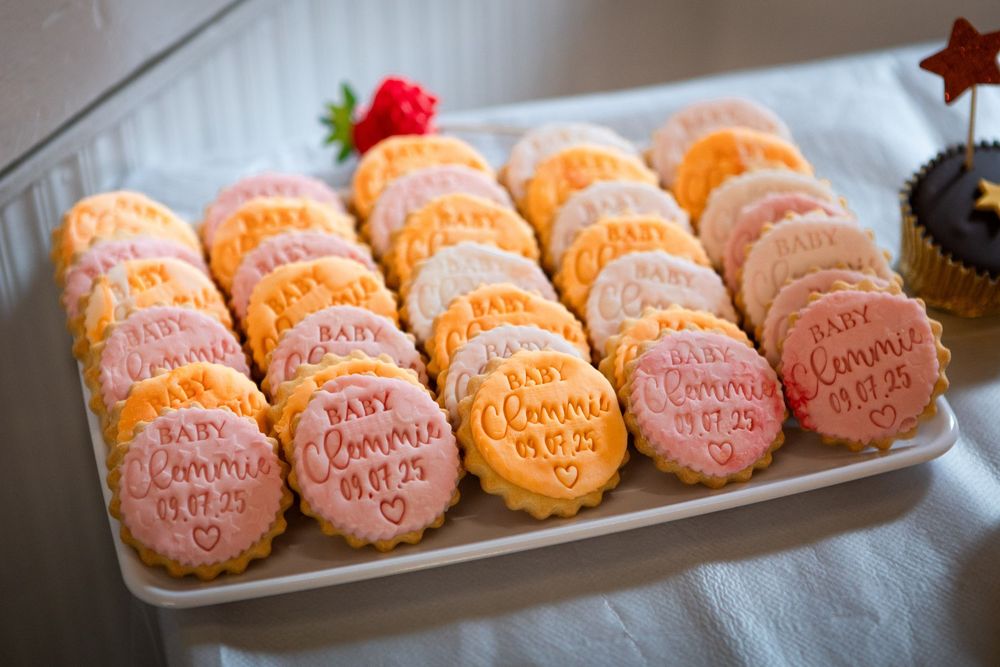 Personalized baby shower cookies reading Baby Connie on a white tray, decorated in pink, orange, and white icing.
