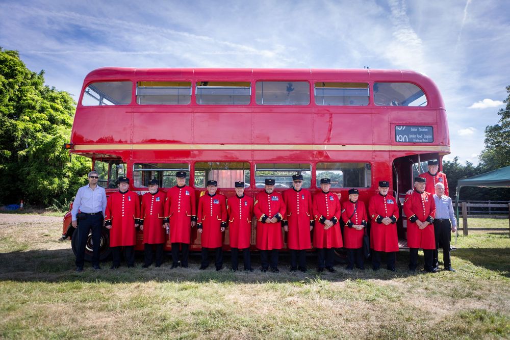 Chelsea Pensioners in red uniforms posing in front of a classic red London double-decker bus outdoors.