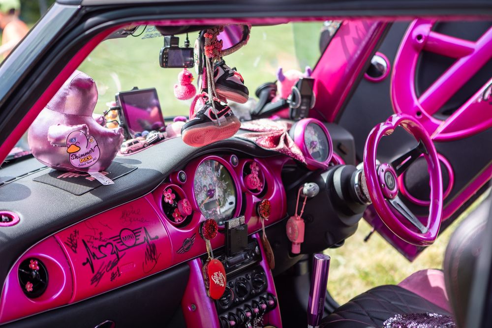 Vibrant pink and magenta custom car interior with decorated dashboard, pink steering wheel, and unique accessories on display.
